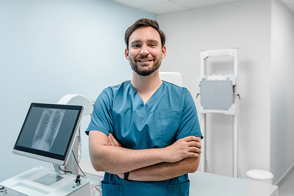 Radiologic technologist smiling and standing with his arms crossed in front of x-ray equipment.